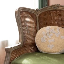 Antique wooden chair with a cane backrest, green cushion, and round beige pillow with an embroidered floral design.