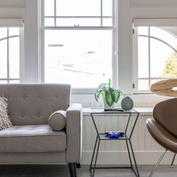 A modern living room with a grey sofa, a brown chair, a small table with plants and decorative items, and large windows with arched panes.