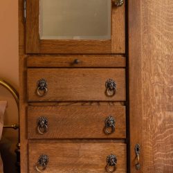 A wooden cabinet with a top glass door and four drawers below, each with ornate metal ring handles.