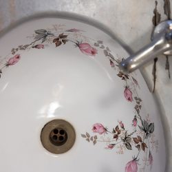 A white ceramic sink with a floral pattern of pink and brown flowers around the basin, paired with a metal faucet.