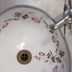 A white ceramic sink with a floral pattern of pink and brown flowers around the basin, paired with a metal faucet.